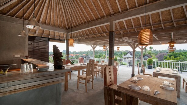 An outdoor dining area with wooden tables and chairs, hanging lights, and a view of the landscape. - Kememai Hostel (Ubud)
