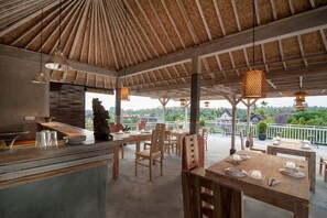 Un espace de restauration en plein air avec des tables et des chaises en bois, des lampes suspendues et une vue sur le paysage.