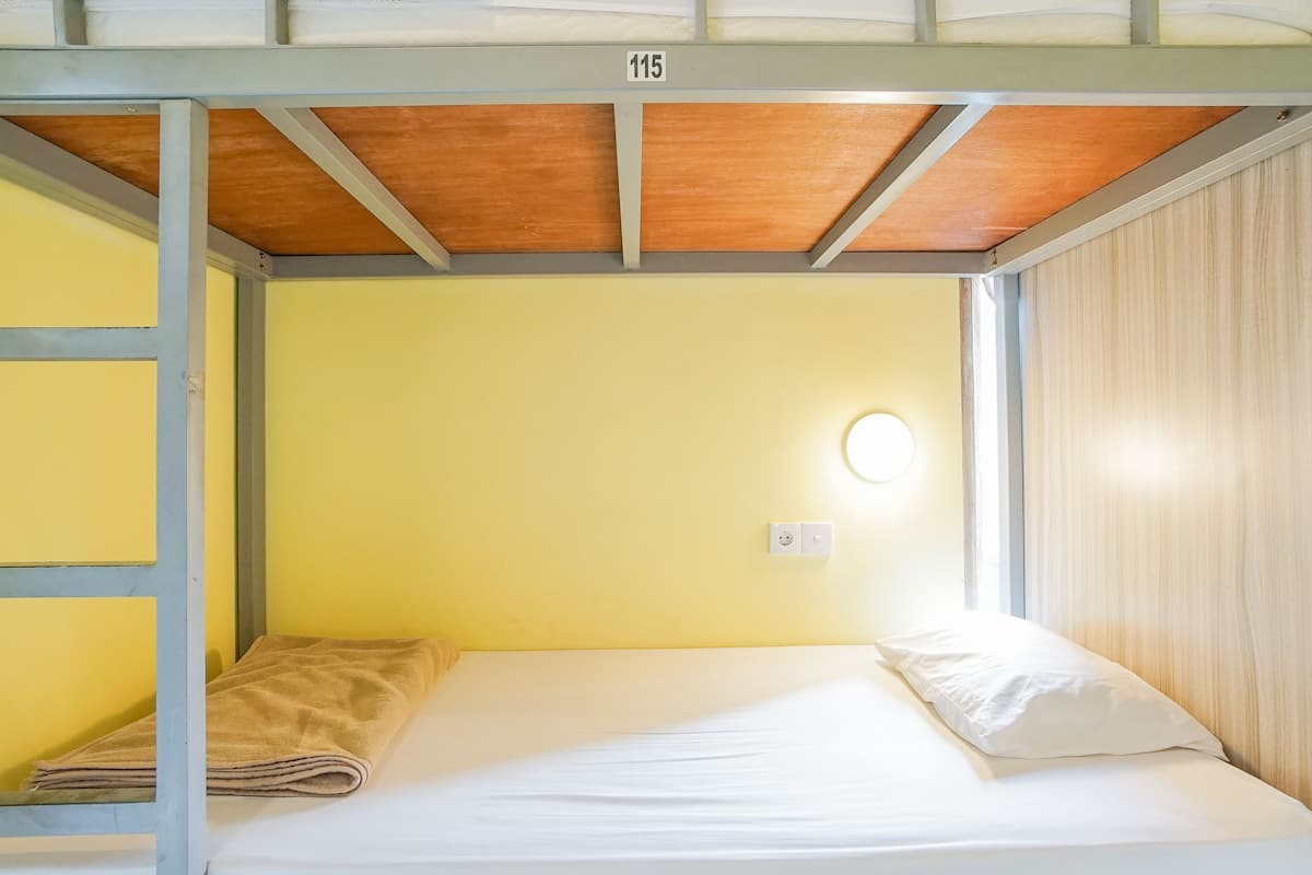 A single bed with a white mattress and pillow in a room with yellow walls and a wooden ceiling.