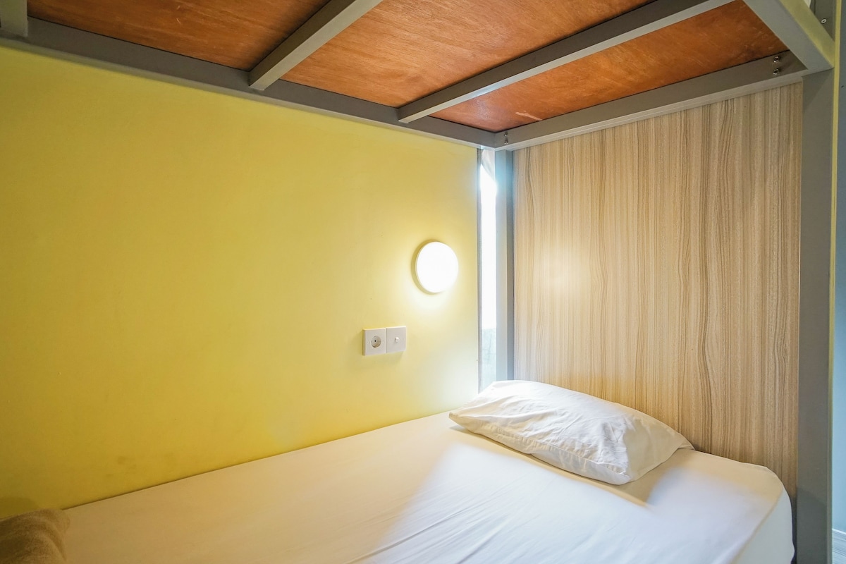 A single bed with a white mattress and pillow in a room with yellow walls and a wooden ceiling.