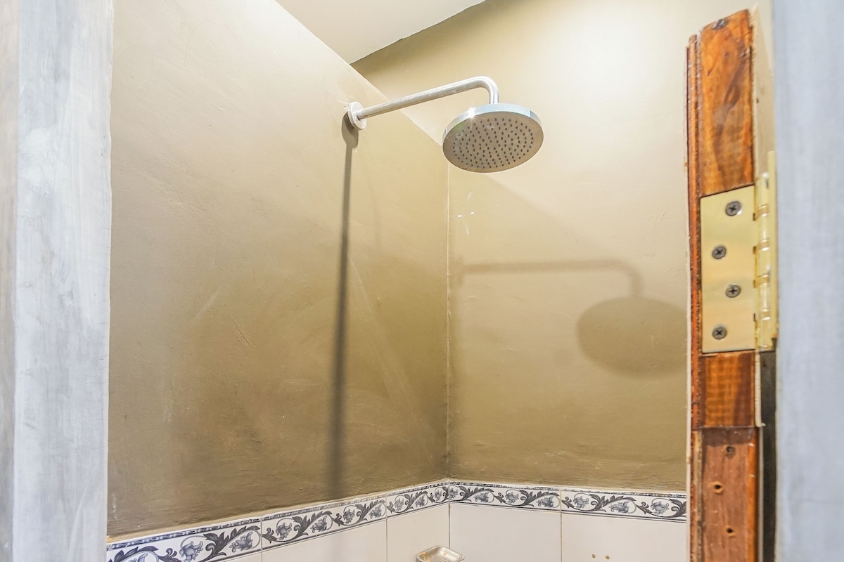 Ducha con cabezal de ducha manual, suelo de baldosas y un rincón con detalle decorativo.