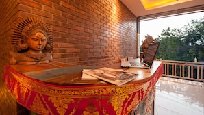 A reception desk with a laptop, a magazine, and a decorative bust against a brick wall. - Kememai Hostel (Ubud)