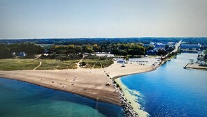 An aerial view of a coastal area with a beach, a marina, and a residential area with houses and trees. - 'Stones Throw' Lakeside Home - Walk to Marina + Town + Assoc Beach (New Buffalo)