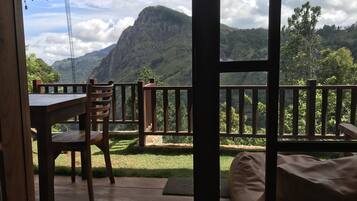 Un balcón con una mesa y sillas de madera, un banco acolchado y vistas a un paisaje montañoso.