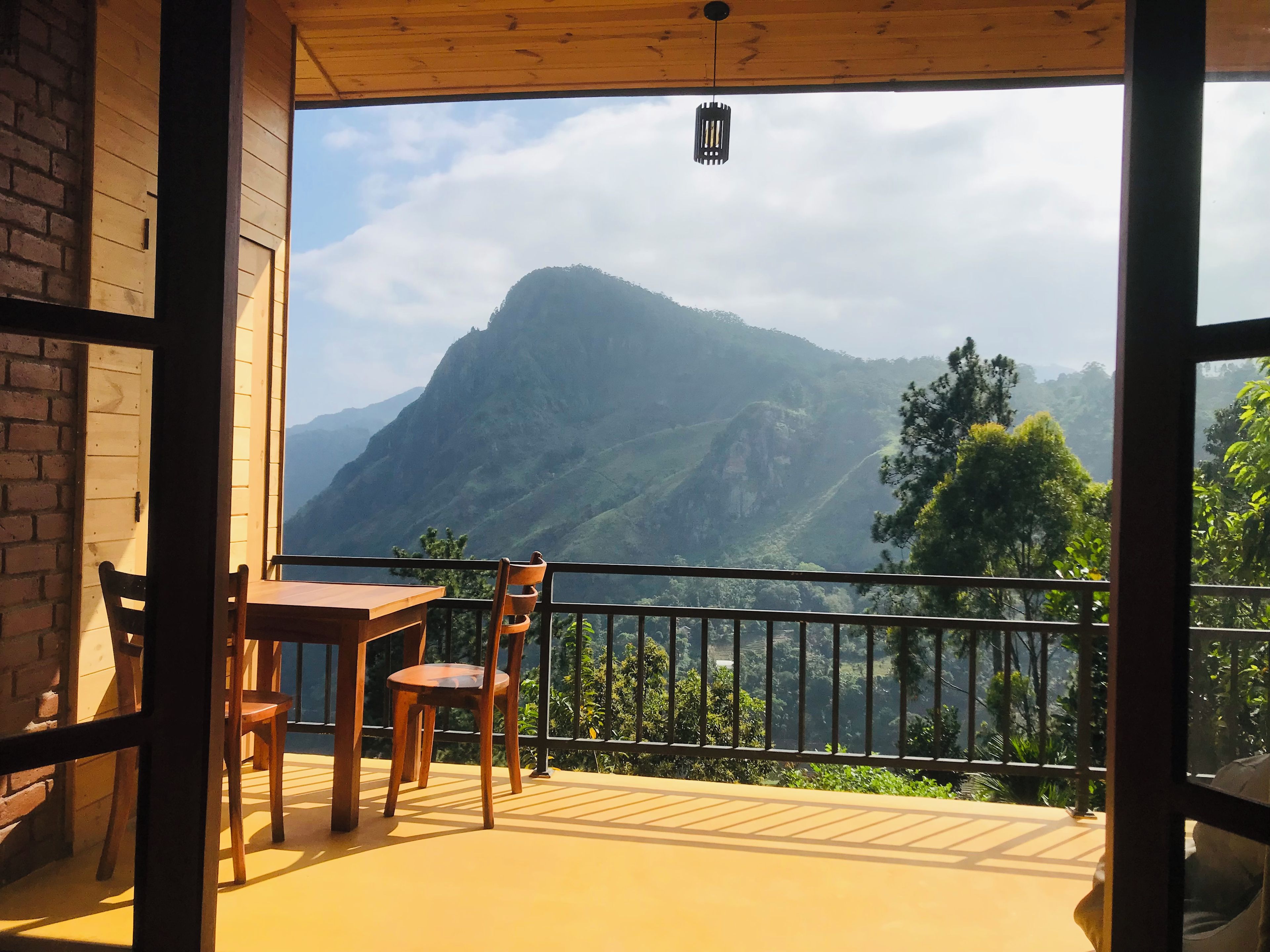 A balcony with a table and chairs, offering a view of a mountain range.