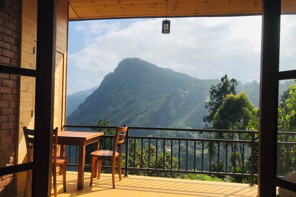 A balcony with a table and chairs, offering a view of a mountain range.