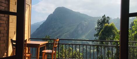 A balcony with a table and chairs, offering a view of a mountain range.