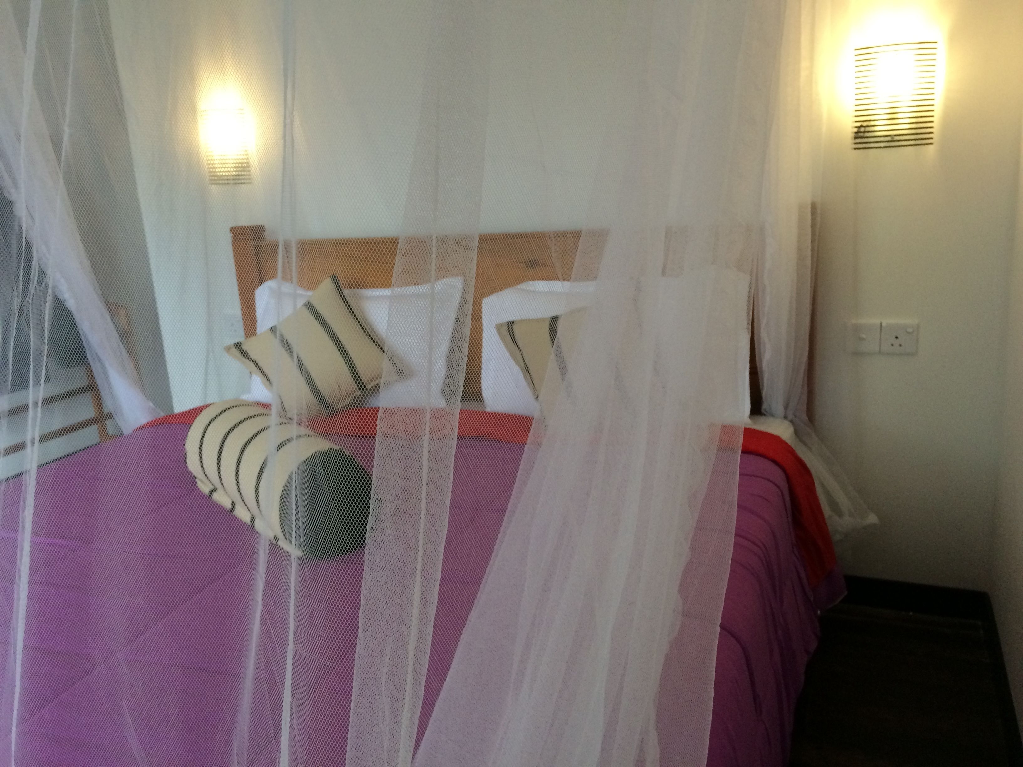 Una cama con dosel, almohadas y una colcha a rayas rojas y blancas.