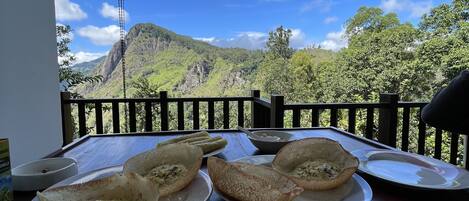 Ein Frühstückstisch mit Speisen, Geschirr und Besteck, mit Blick auf Berge und grüne Landschaft.
