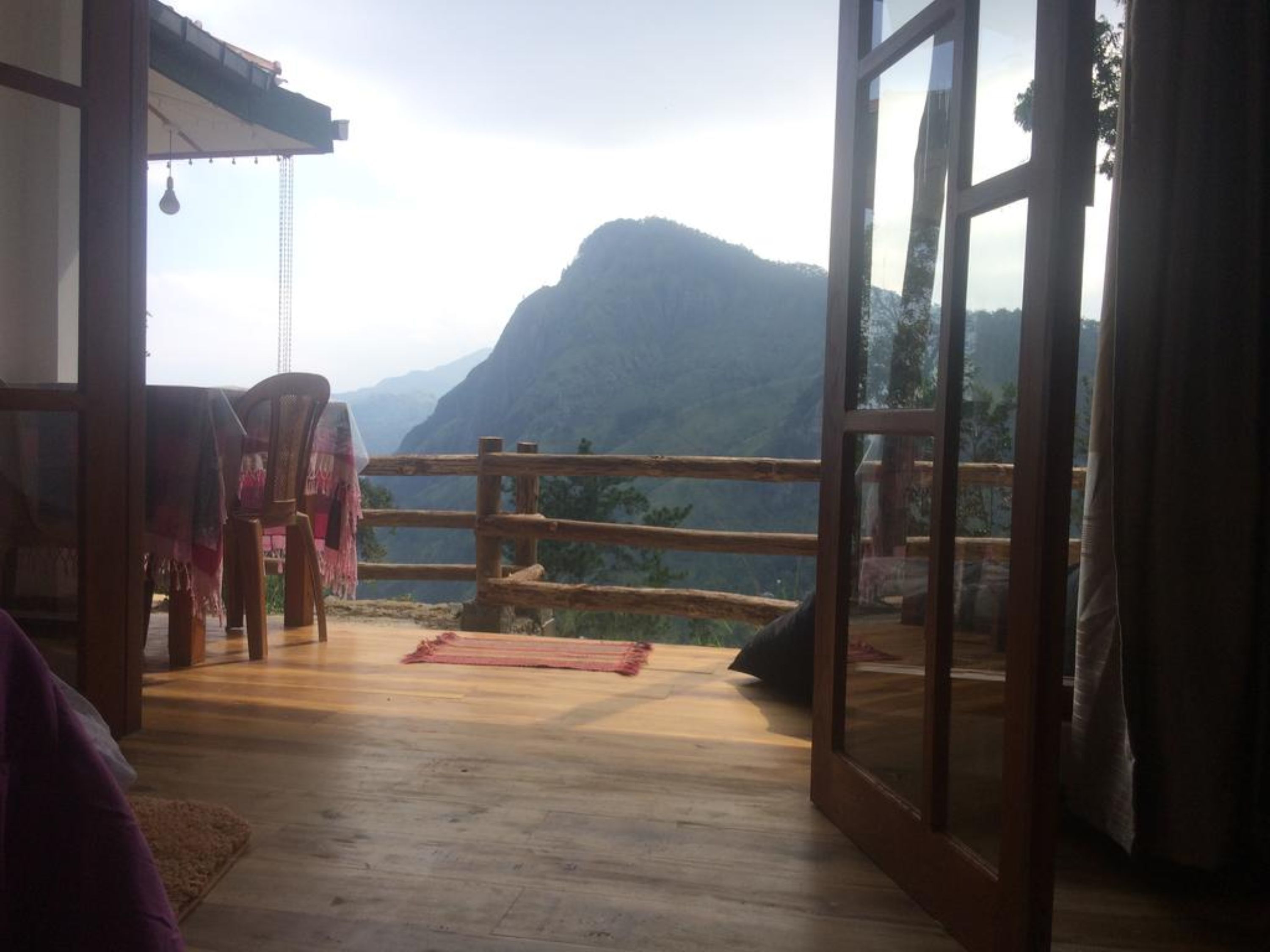 Una habitación con suelo de madera, vista a una montaña y barandilla de madera.
