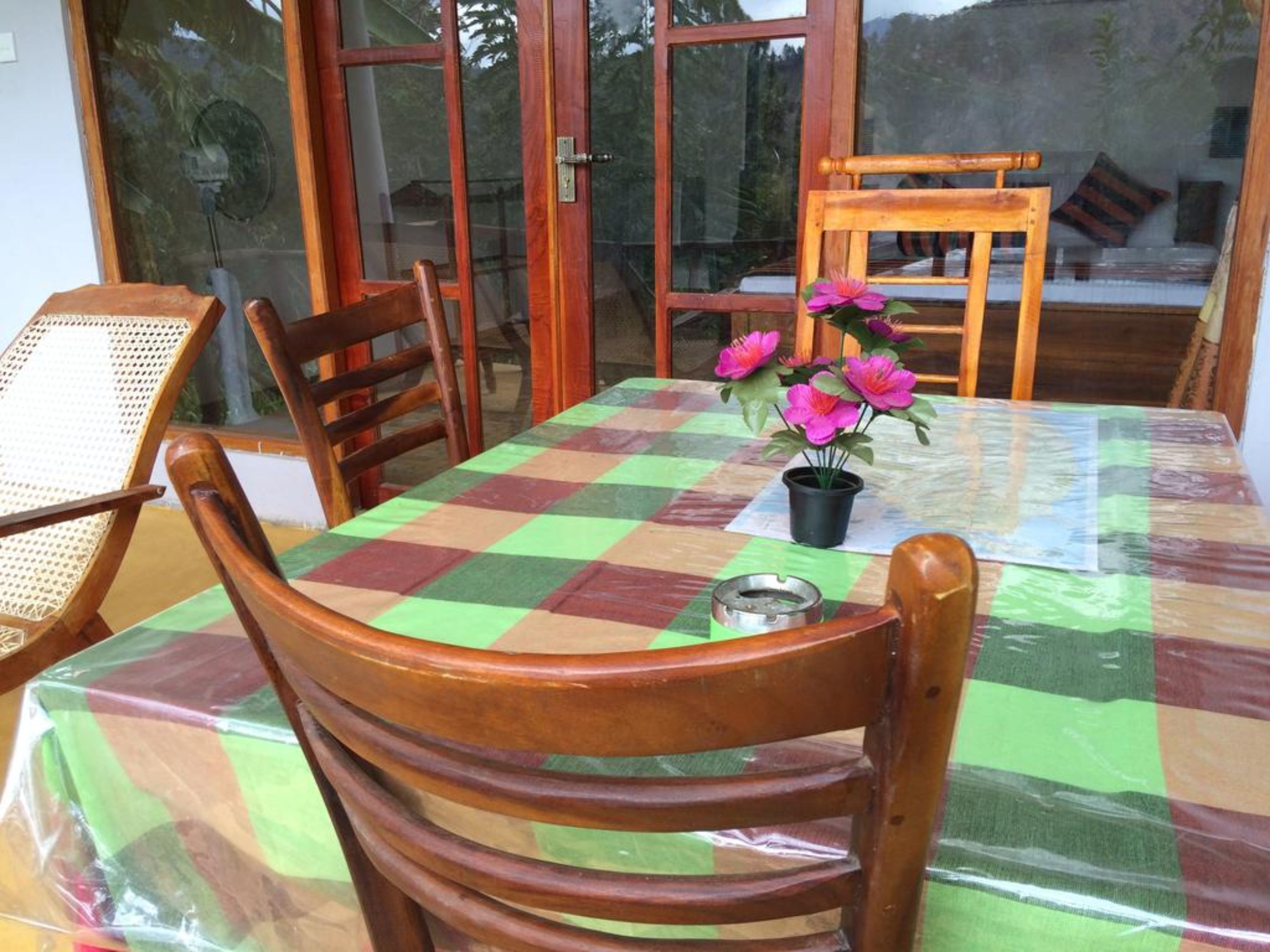 A dining area with a checkered tablecloth, wooden chairs, and a potted plant with pink flowers.