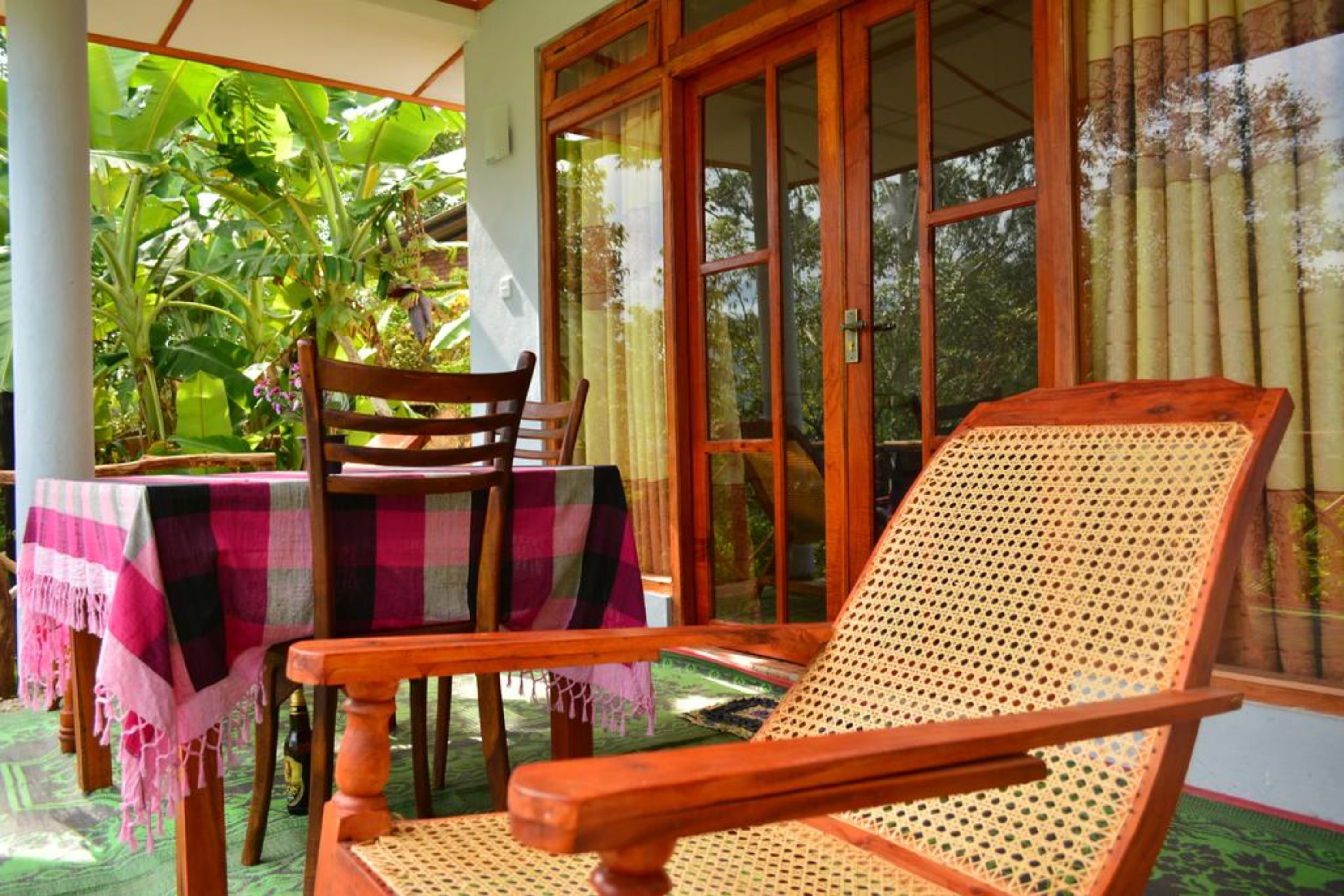 A wooden chair and table set on a veranda with a view of lush greenery.