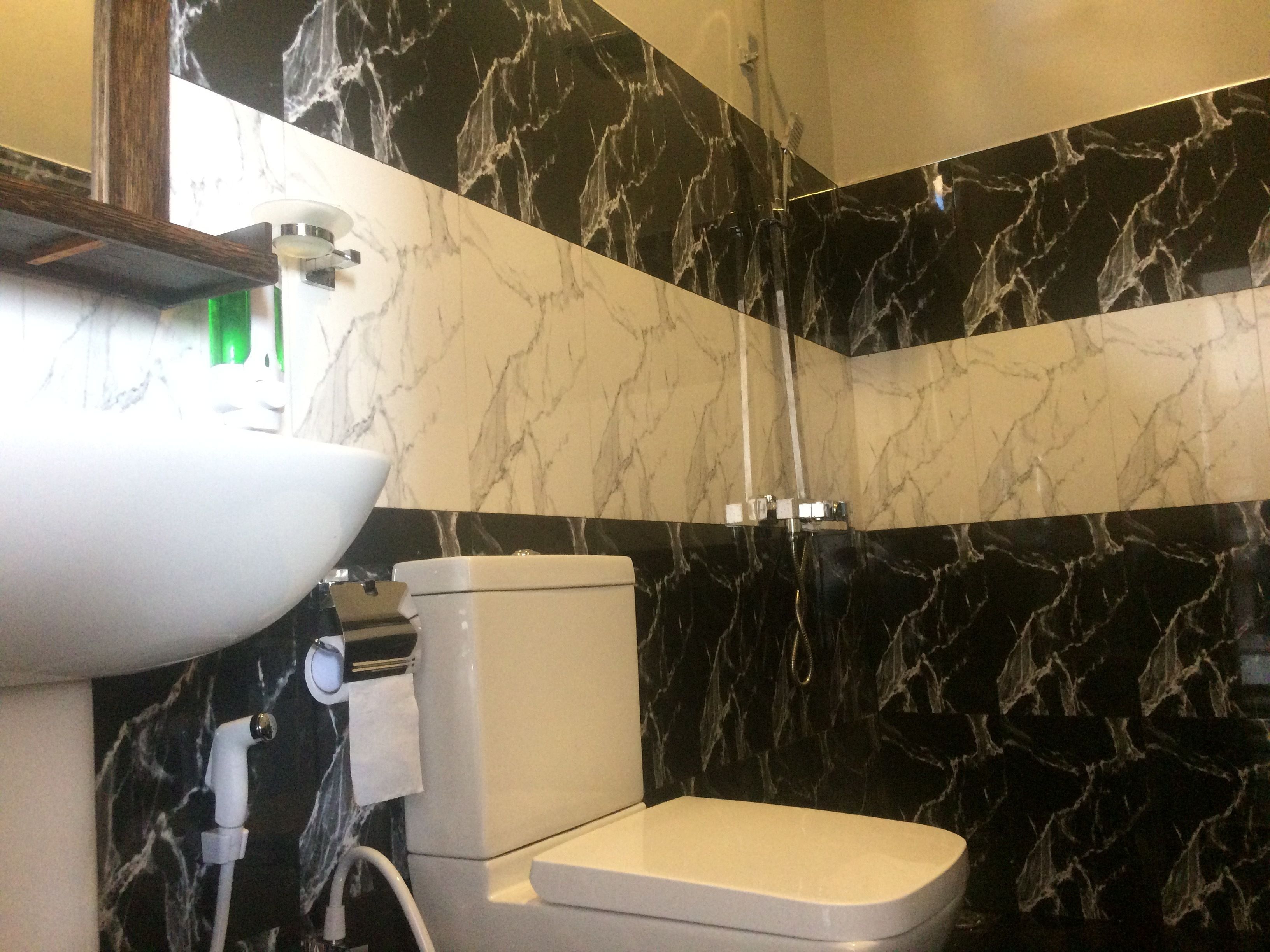 A bathroom with a white sink, toilet, and shower. The walls are covered in black marble with white veining.