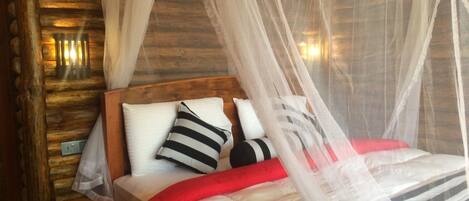A bed with a canopy, pillows, and a red blanket in a room with wooden walls and a nightstand.