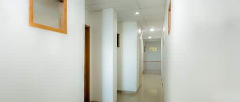 Un pasillo limpio y bien iluminado, con paredes blancas y suelo de baldosas, que conduce a una habitación con papel tapiz decorativo y barandilla.