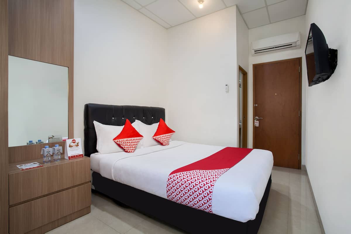 Een hotelkamer met een bed, een houten nachtkastje, een spiegel en een aan de muur bevestigde televisie.