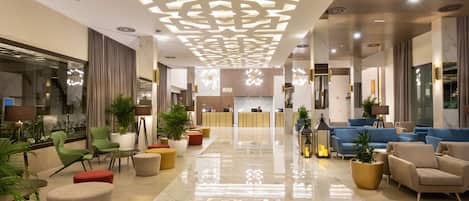 Un moderno vestíbulo de hotel con una recepción, áreas de descanso e iluminación decorativa.