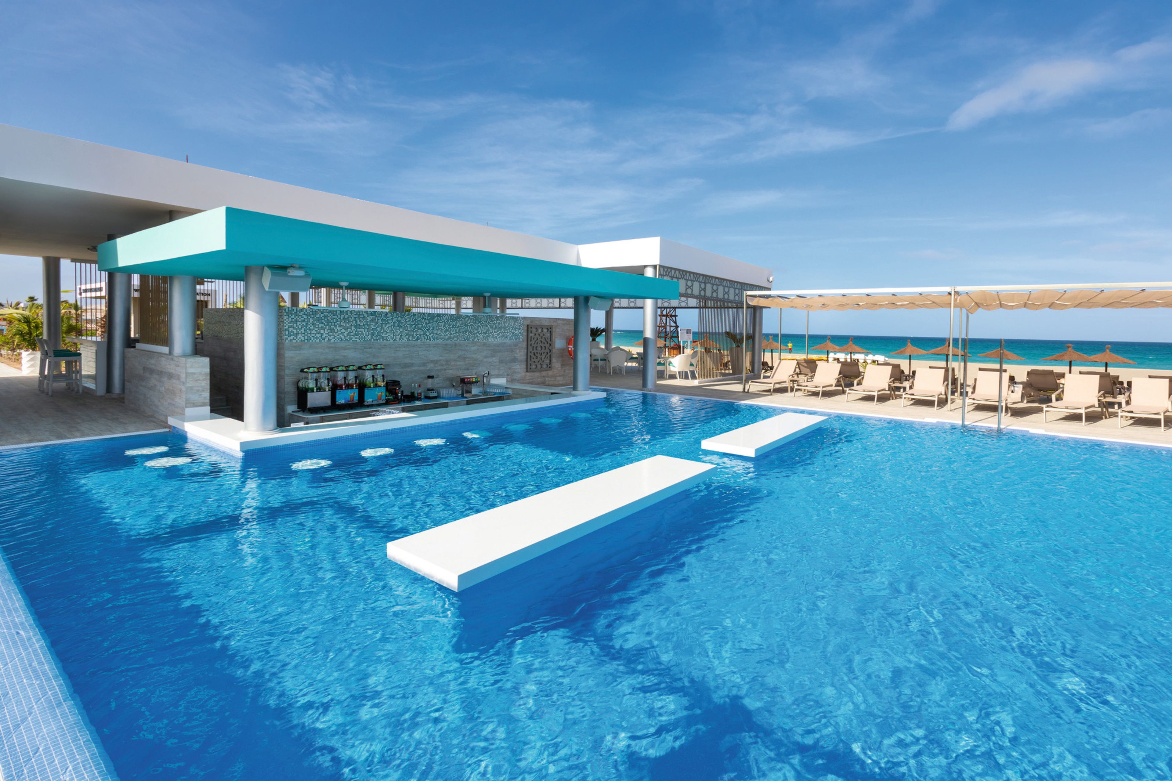 A modern infinity pool with a bar area and lounge chairs facing the ocean.