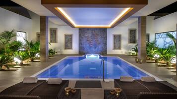 Una piscina interior moderna con sillas de descanso y plantas en macetas.