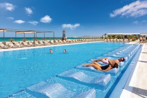 Una piscina con sillones de descanso y sombrillas, una torre de salvavidas y una vista despejada del océano.