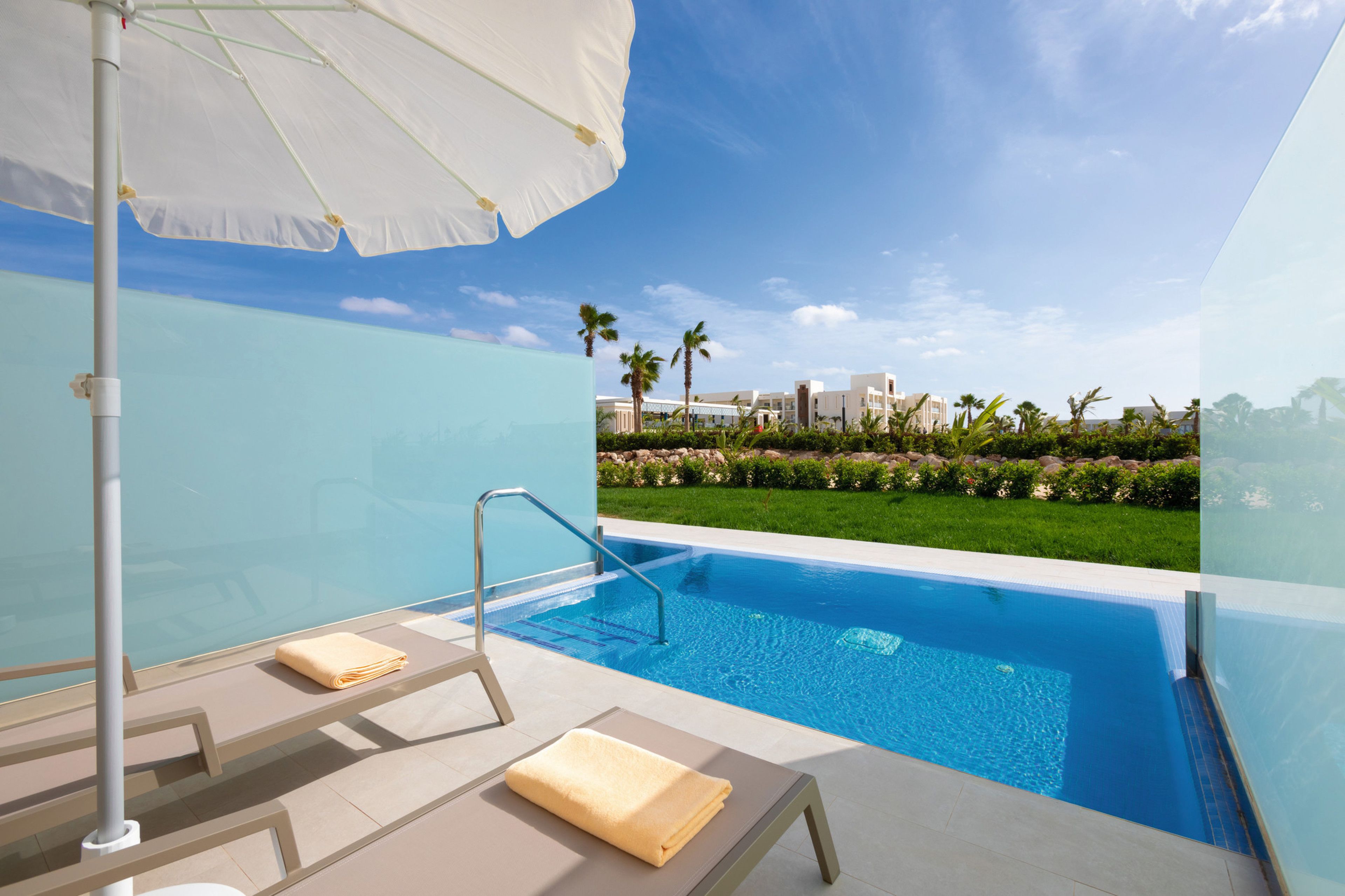A modern pool area with clear blue water, lounge chairs, and an umbrella.