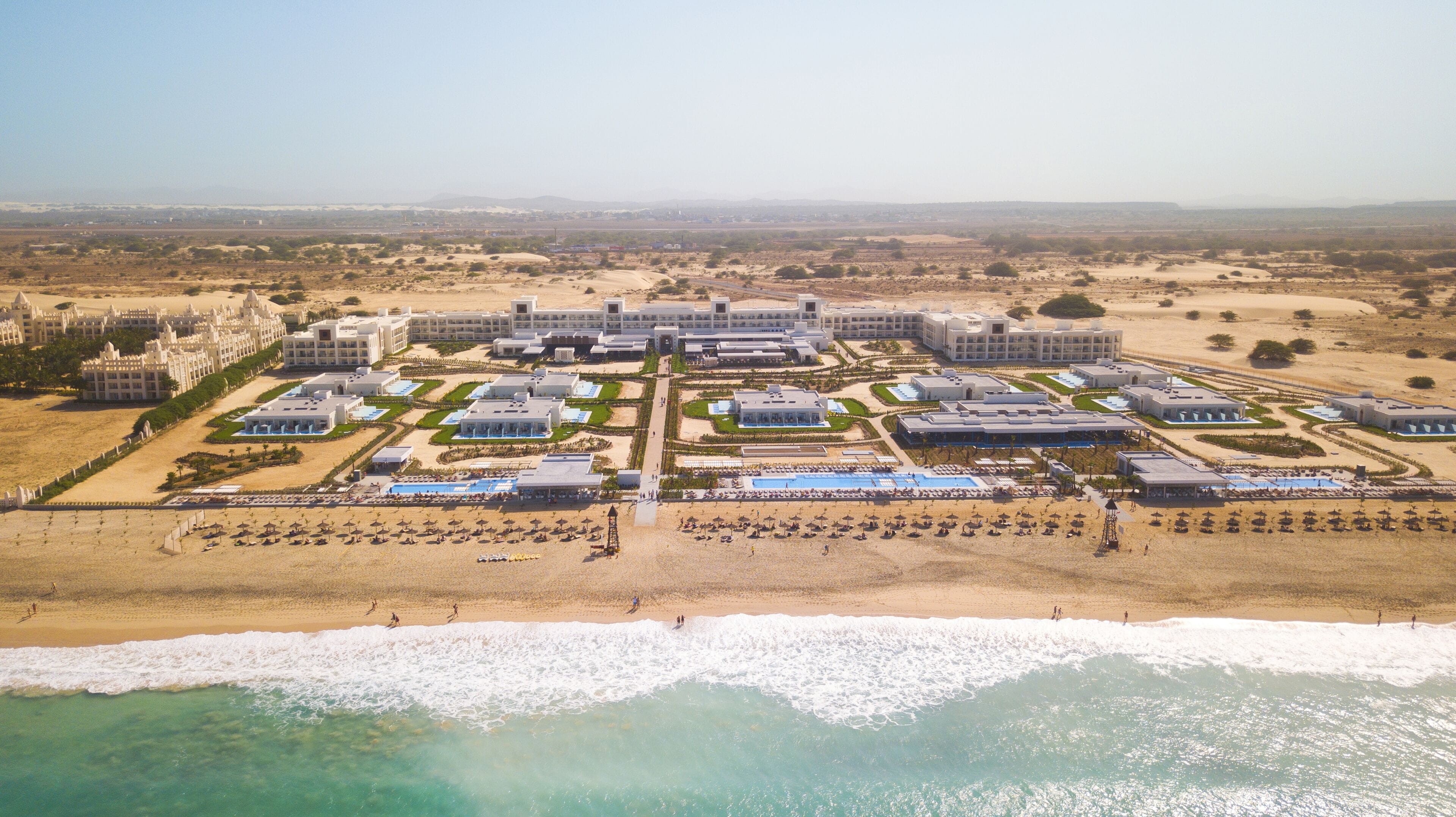 An aerial view of a resort with multiple buildings, a beachfront, and a swimming pool area.