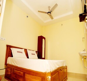 Quarto de hotel com uma cama de madeira, um ventilador de teto e um pequeno armário.
