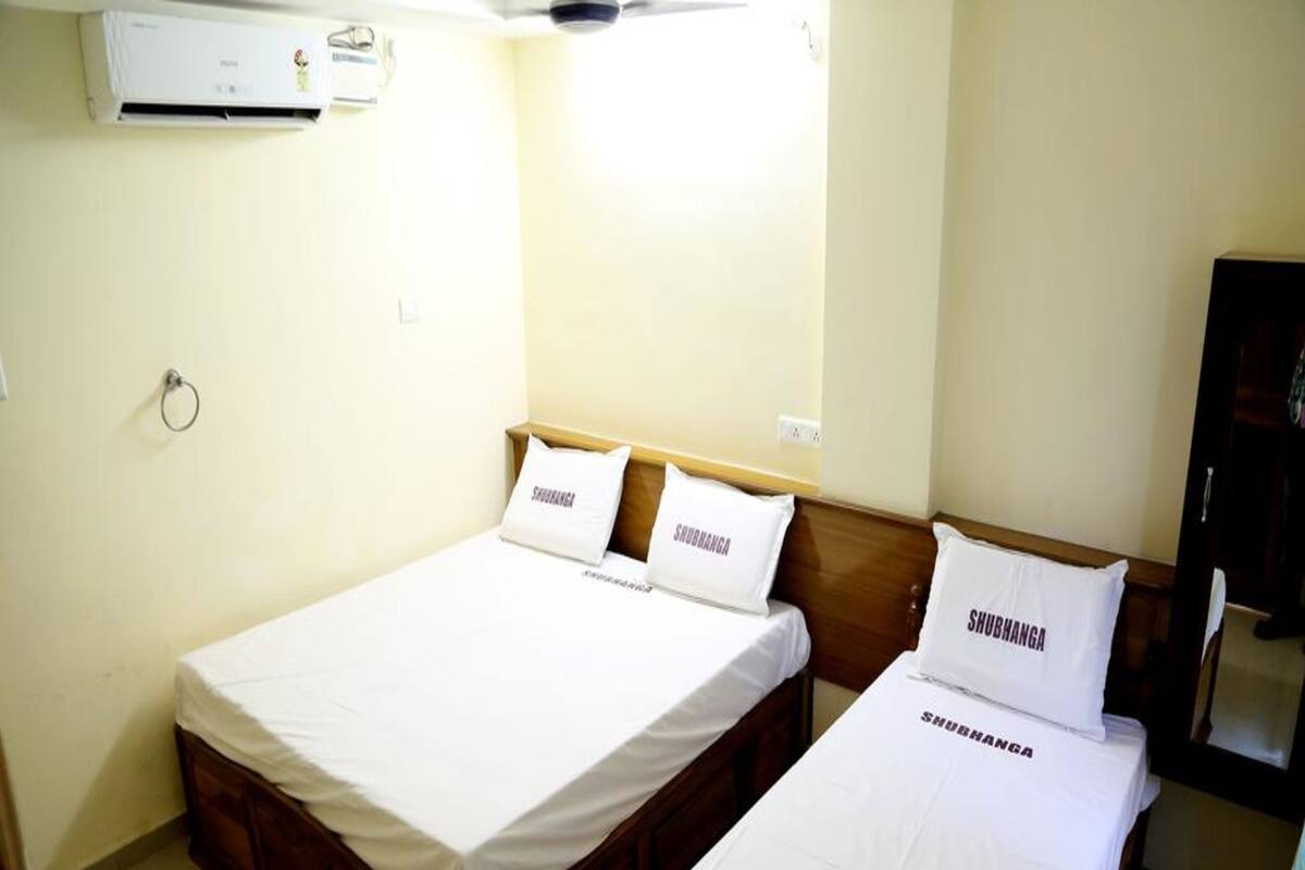 A hotel room with two single beds, each with a pillow labeled "SHUBHANGA".