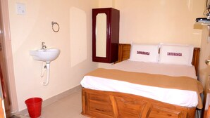 A bedroom with a wooden bed, a white sink, and a mirror. - Hotel Shubhanga Residency (Srikalahasti)