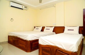 A room with two wooden beds, each with a white mattress and pillows labeled "SHUBHANGA". An air conditioning unit is mounted on the wall above the beds. - Hotel Shubhanga Residency (Srikalahasti)