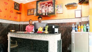 A reception desk with a computer, a refrigerator stocked with beverages, and religious artwork on the walls. - Hotel Shubhanga Residency (Srikalahasti)