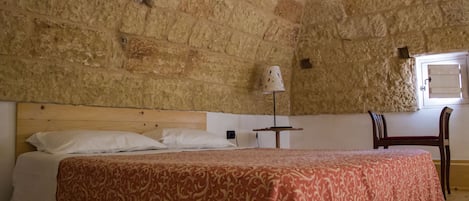 Quarto com uma cama grande, cabeceira de madeira, uma mesinha com abajur e uma cadeira.