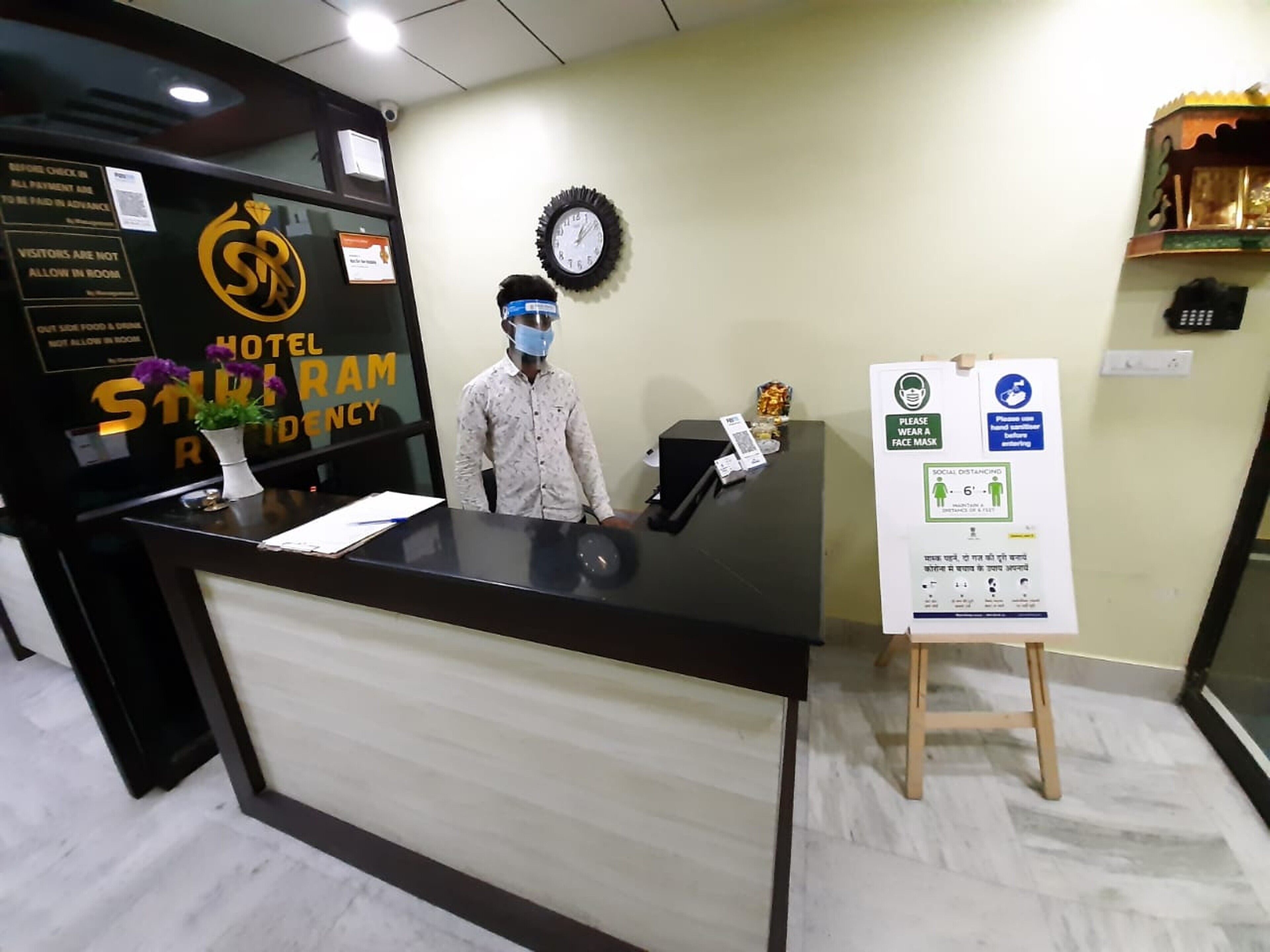 A hotel reception desk with a sign indicating social distancing and mask-wearing.