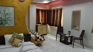 A hotel room with a bed, a desk, a chair, a small table, a mirror, and a window with curtains.
