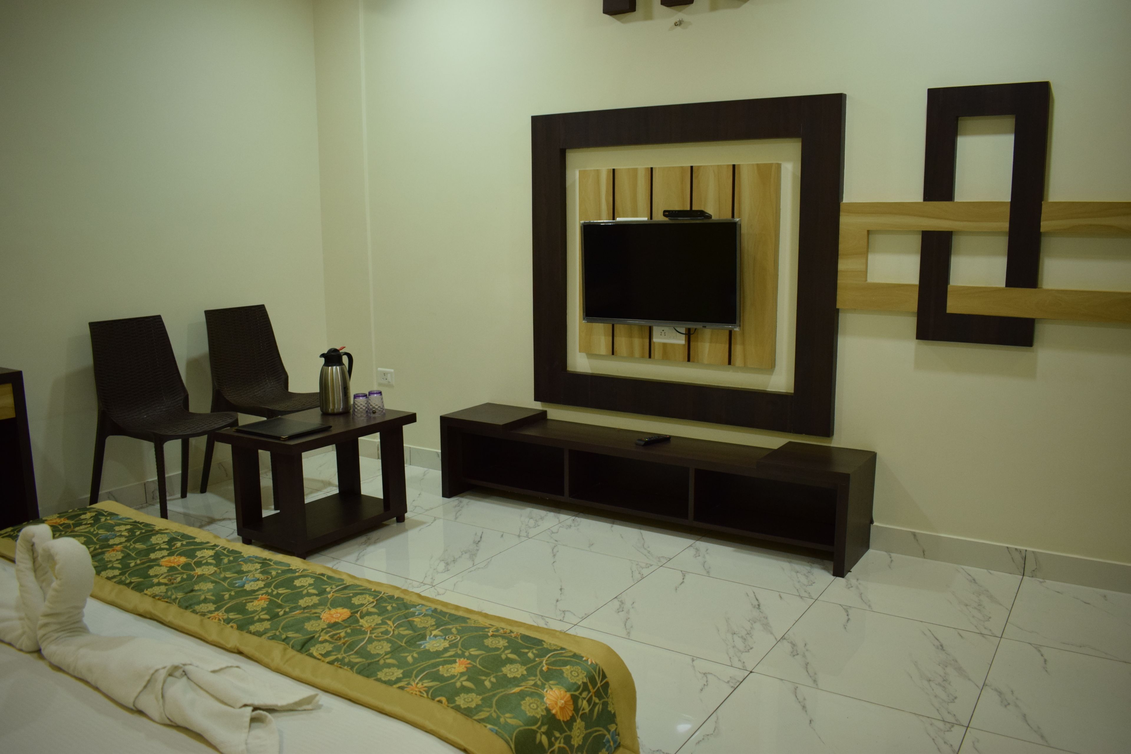 A hotel room with a bed, a TV mounted on the wall, a coffee table, and two chairs.