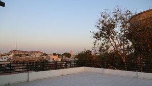 A rooftop terrace with a tiled floor, a black railing, and a view of a cityscape including buildings and a hill.