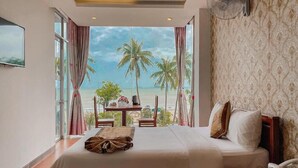 A bedroom with a bed, a bedside table, a fan, and a view of the beach. - Y Linh Hotel (Quy Nhon)