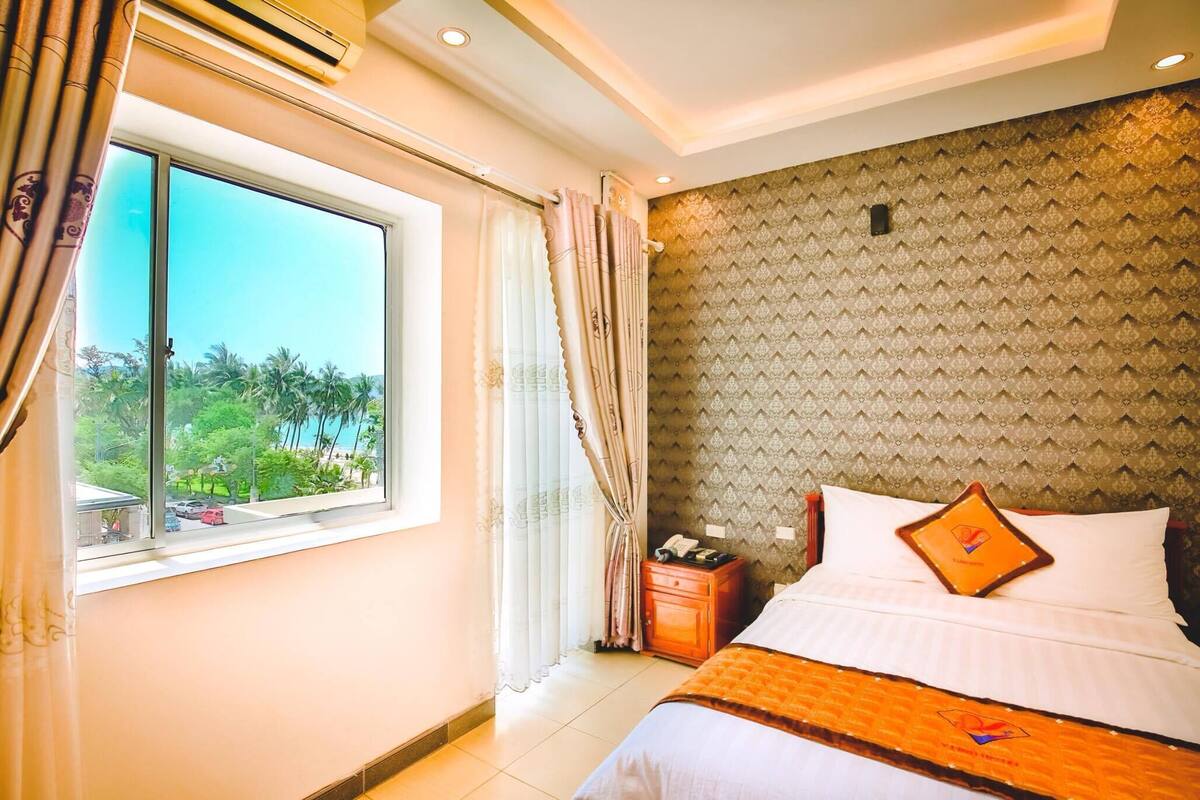 A hotel room with a bed, a nightstand, a window with curtains, and a patterned wall.