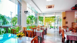 A modern restaurant with glass tables and chairs, large windows, and a view of greenery outside. - Y Linh Hotel (Quy Nhon)