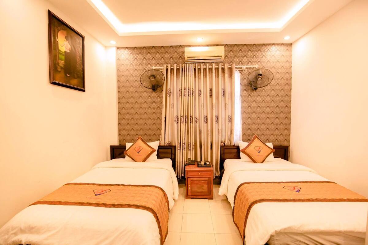 A hotel room with two beds, a ceiling fan, an air conditioner, and a decorative curtain.