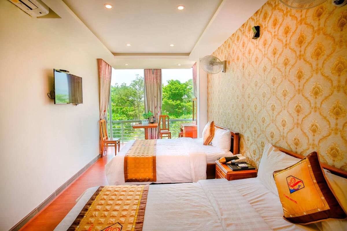 A hotel room with two beds, a TV, a balcony with a table and chairs, and a patterned wallpaper.