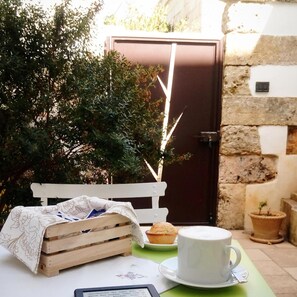 Una mesa con una taza y platillo blancos, un muffin y una cesta de pan sobre un mantel verde.