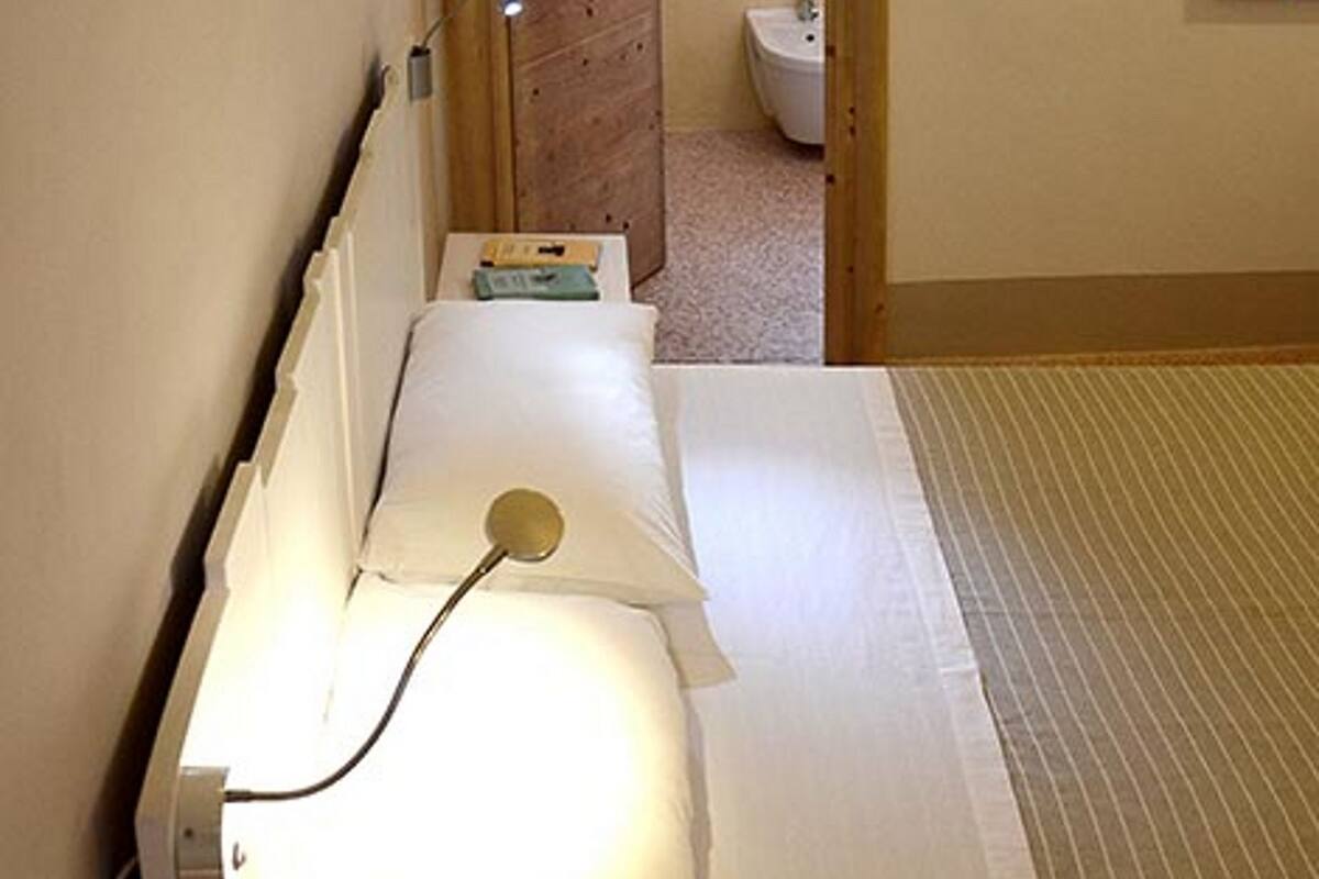 A narrow hotel room with a bed, a bedside lamp, and a view into the bathroom.