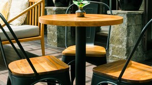 A round wooden table with chairs, potted plants, and a stone wall in a modern interior setting. - Umpadhi Canggu Hotel (Canggu)