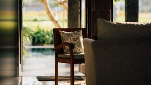 A modern interior with a wooden chair and a sofa near a glass door leading to a garden. - Umpadhi Canggu Hotel (Canggu)
