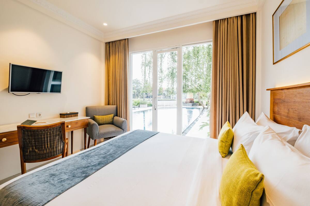 A hotel room with a bed, a desk, a chair, a TV, and a view of the outdoors.
