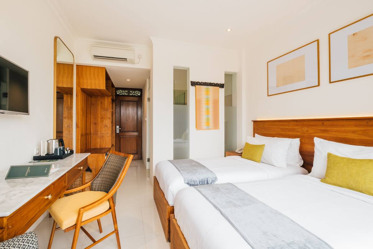 A hotel room with a wooden desk, two beds, a chair, and a TV.