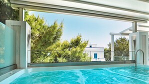 Una piscina interior moderna con agua azul cristalina, ventanas amplias y vistas a árboles y un edificio exterior.