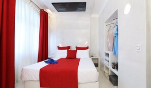 A hotel room with a bed, red curtains, a TV, and a wardrobe.