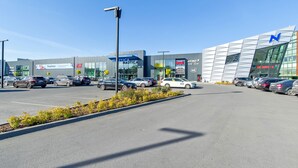 En parkeringsplats med flera bilar och en byggnad med modern design och en stor logotyp i form av bokstaven ”N”.